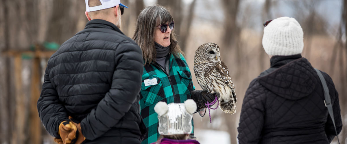 a woman holding a barred owl, with two adults and child watching.