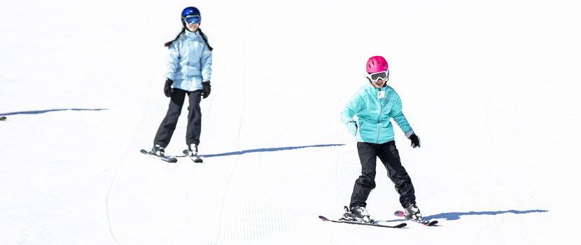 Two girls smile while they ski down a hill.