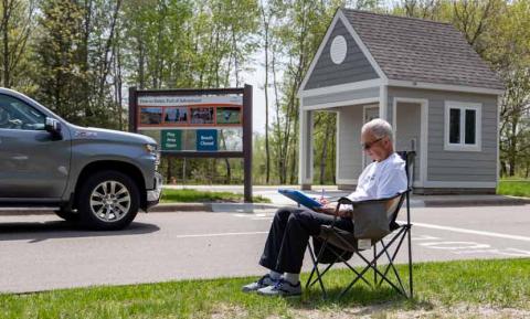 A volunteer sits in a chair on the grass near the vehicle entrance to Bryant Lake Regional Park as part of an observation count.