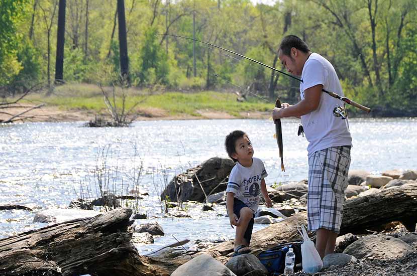 A man and his son fish on the side of a river