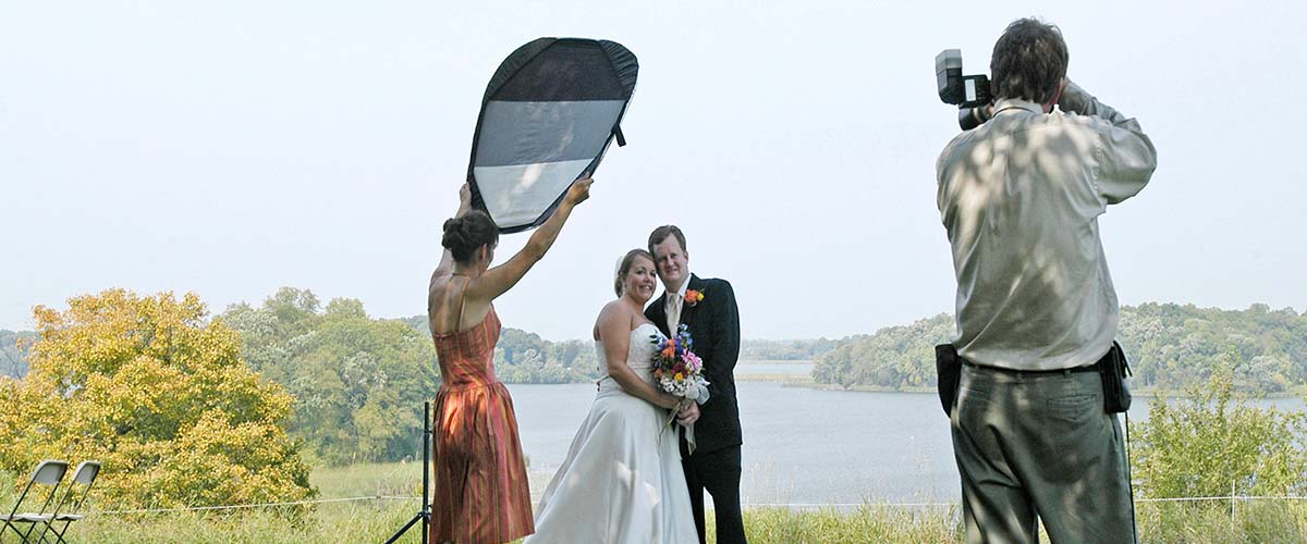 A photographer takes a picture of a bride and groom outside.
