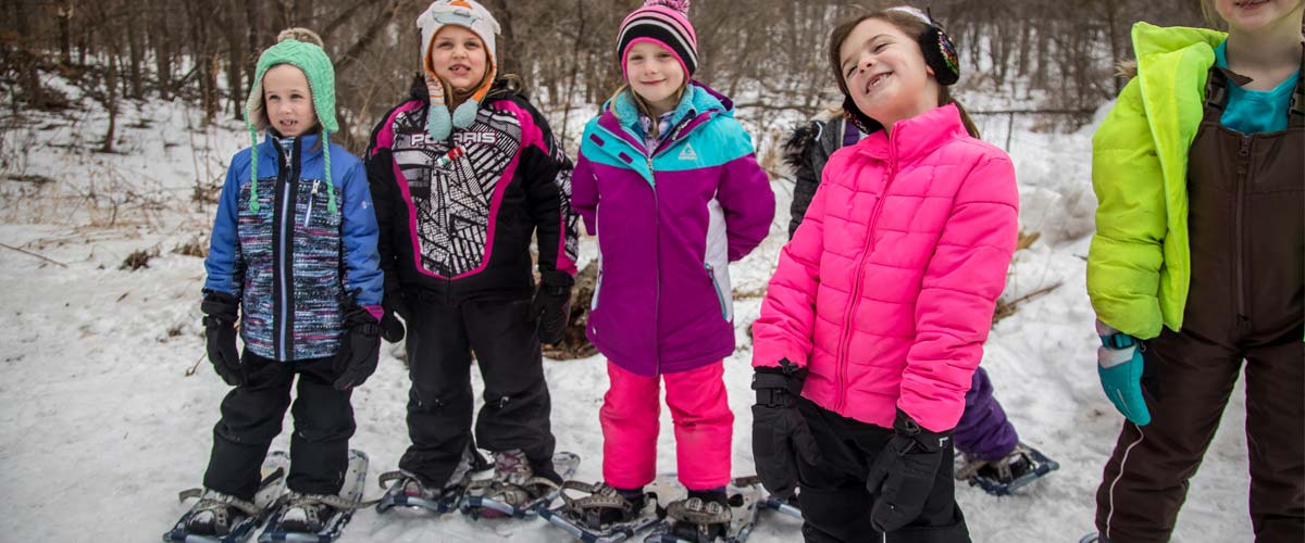 a group of young girls smiling and wearing snowshoes.
