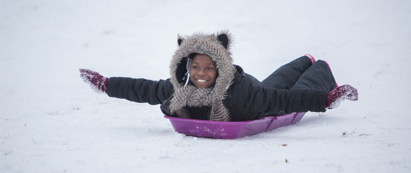 girl sledding on her stomach with her arms extended like an airplane