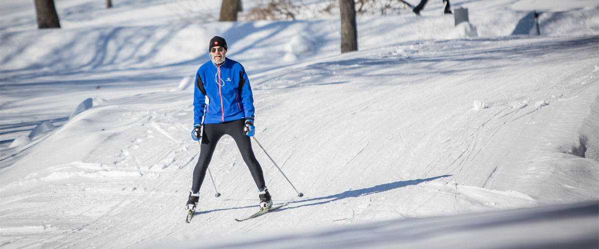 a man in a blue jacket and black pants cross-country skiing down a small hill.