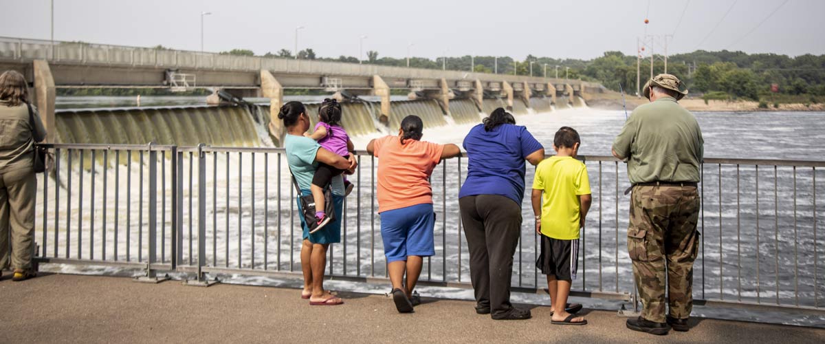 a family standing along a railing in front of the coon rapids dam.