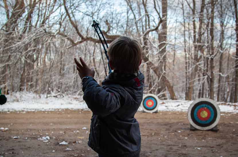 a boy releases an arrow at an archery range in the winter.