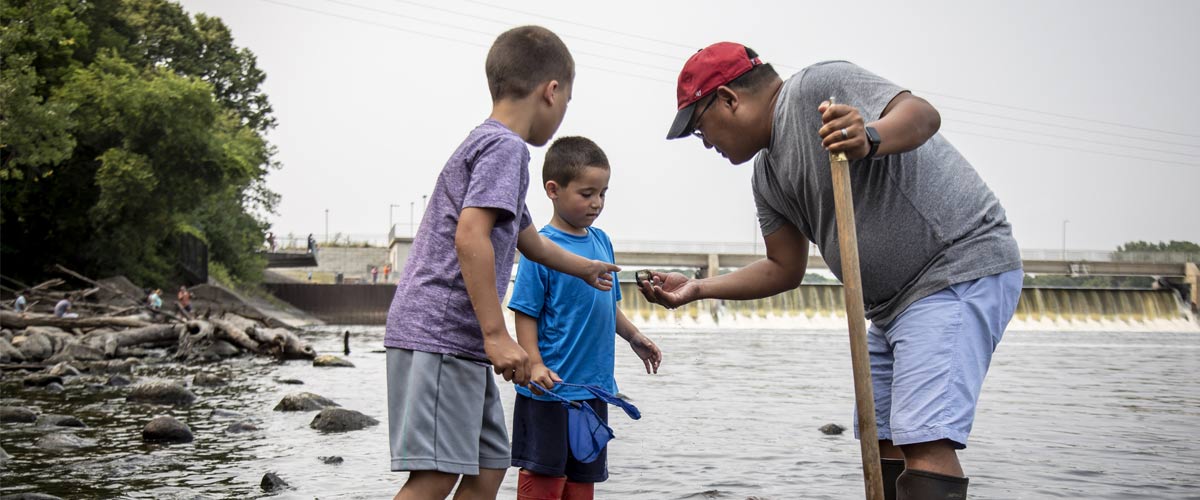 a dad shows his sons something he found while wading in the water. 