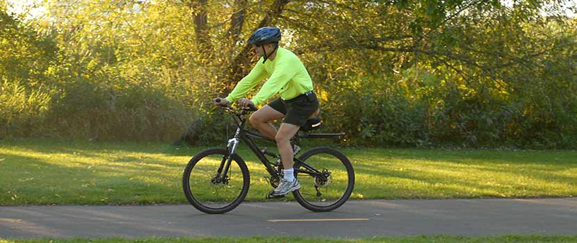 a man biking on a paved trail in the summer or fall.