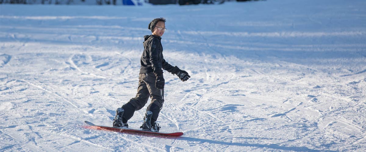 a boy in a black jacket and pants snowboarding down a gentle hill.