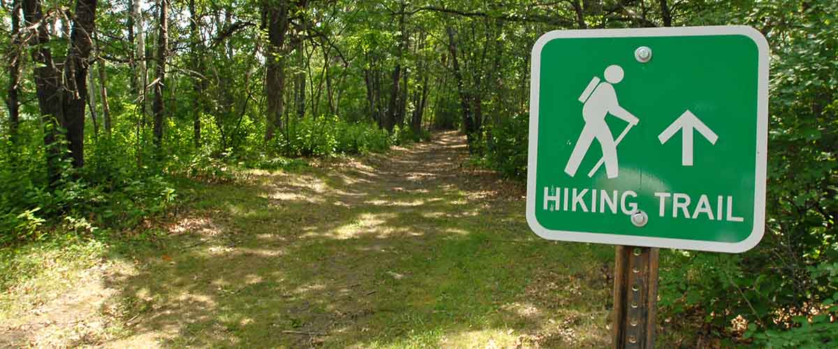 a sign that says hiking trail with a symbol of a hiker. A wooded path can be seen behind it.