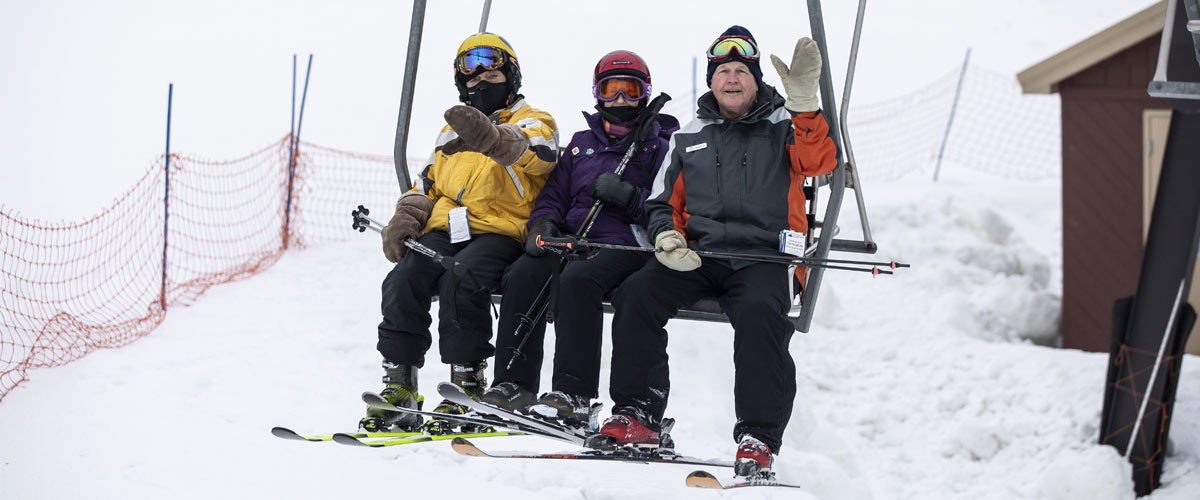 Three older people on a chairlift waiving at the camera.