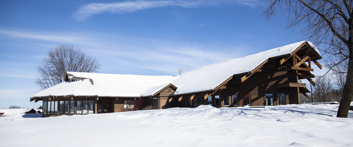 a large brown chalet-type building in the snow against a blue sky.