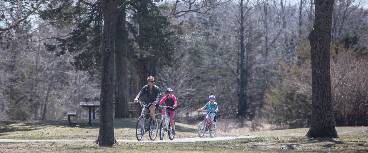 a man and two children biking through an open area with some trees.
