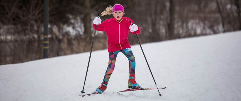 a blonde girl in a pink coat cross-country skiing. 