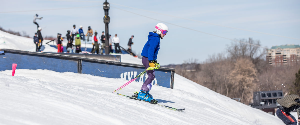 A girl in a white helmet and blue jacket skis down a hill.