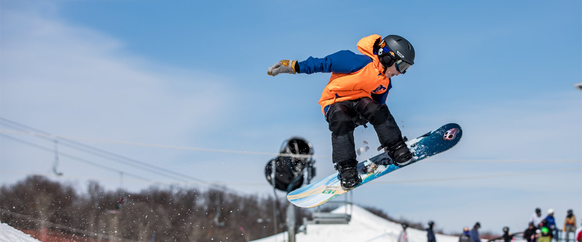 a snowboarder flies through the air against a blue sky. 
