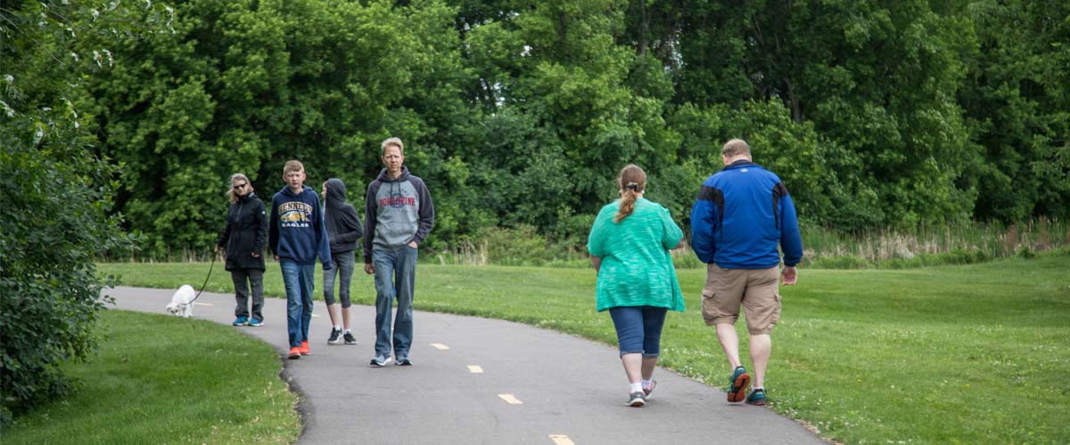 people walk in both directions on a paved trail in the summer.