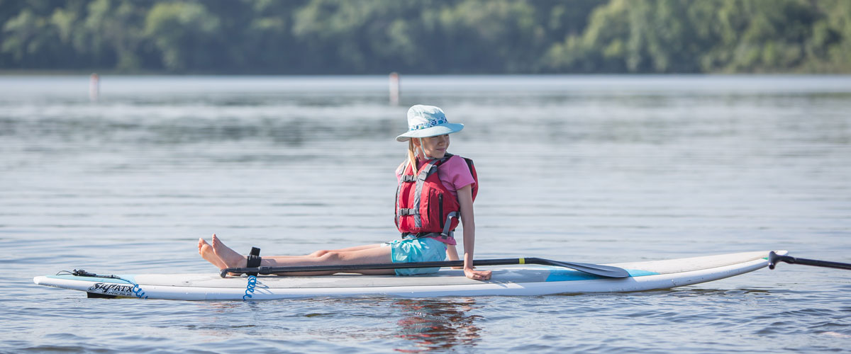 a girl sits on a stand-up paddleboard in the middle of a lake. 