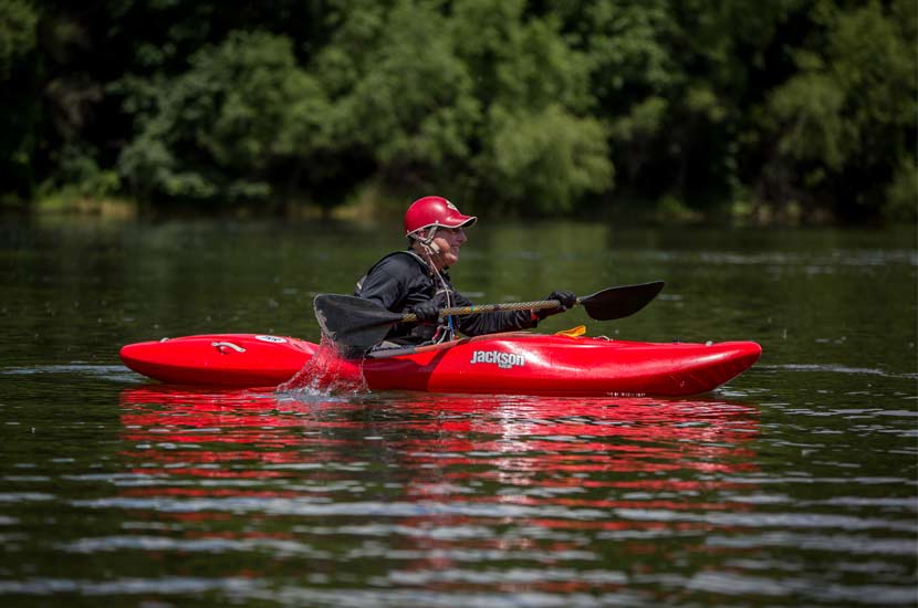 A man in a red hat paddles a red kayak on the water.