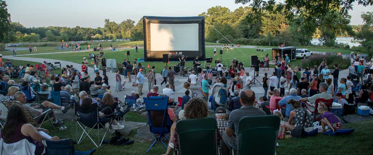 a crowd gathers in an outdoor amphitheater to watch a movie on an inflatable screen.
