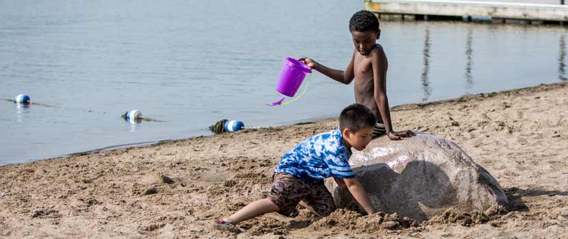 Two boys play with sand toys on a beach.