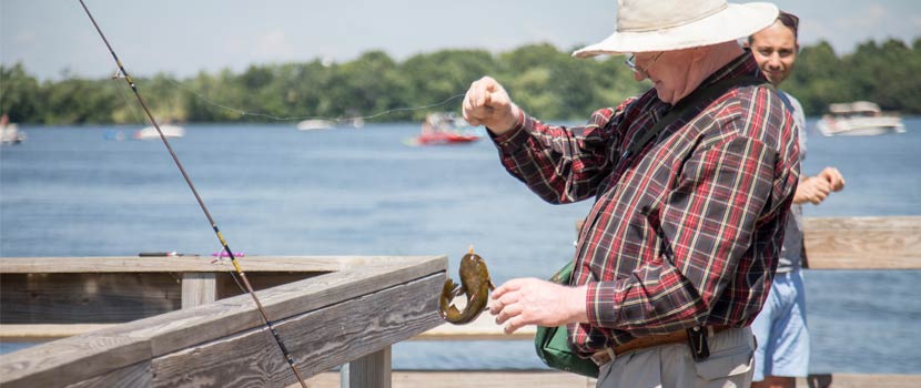 an older man reaches for a fish he caught off a wooden pier.