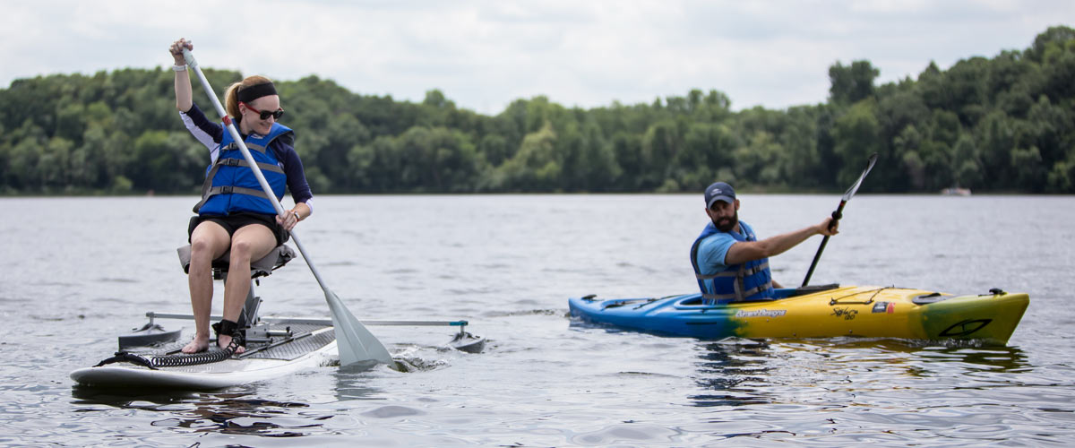 a woman paddles an adapted kayak next to a man in a kayak.