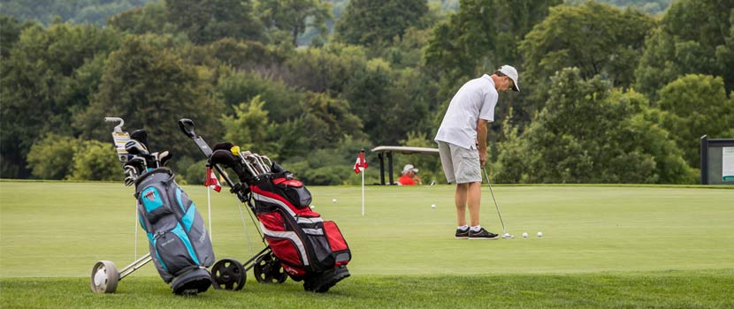 A man golfs on a course. Two golf bags are in the foreground.
