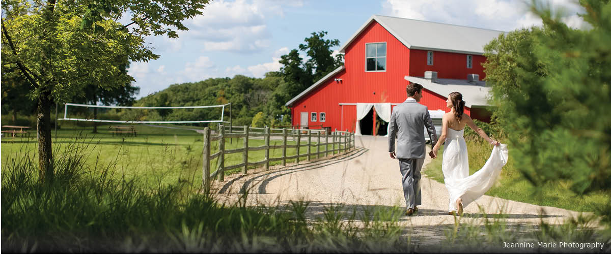 A bride and groom walk toward a red barn.