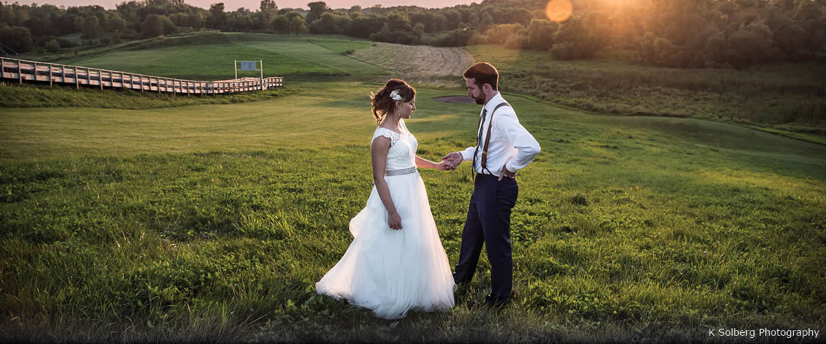 A bride and groom pose for a photo in the grass at sunset.
