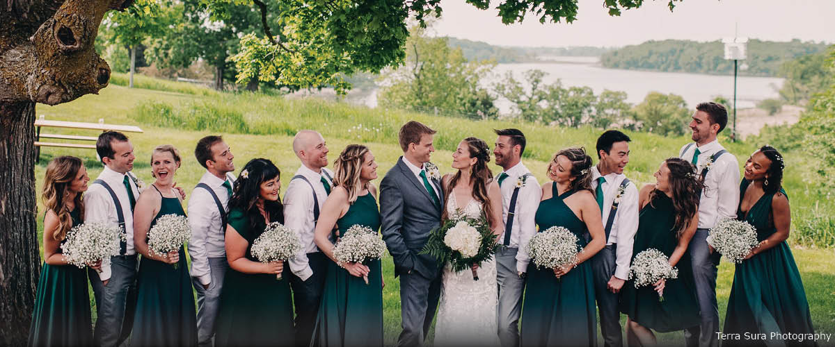 A wedding party poses in front of an overlook above a lake.