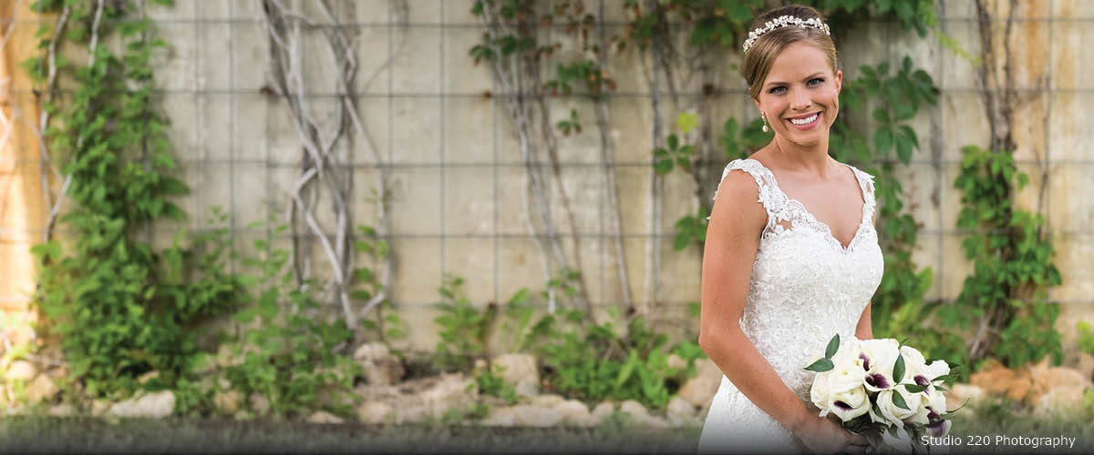 A bride poses in front of a vine-covered wall outside.