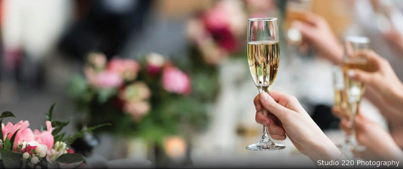 A hand holds up a glass of champagne over a head table at a wedding.