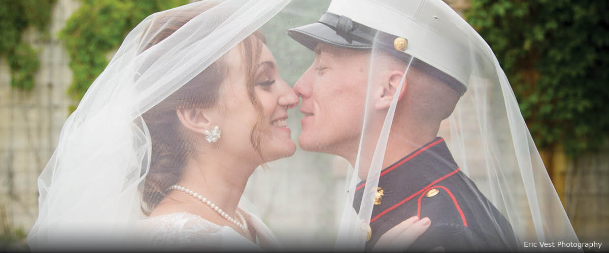 A bride and military groom kiss under her veil.