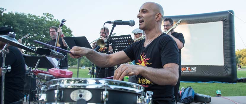A man plays the drums outdoors as part of a band.