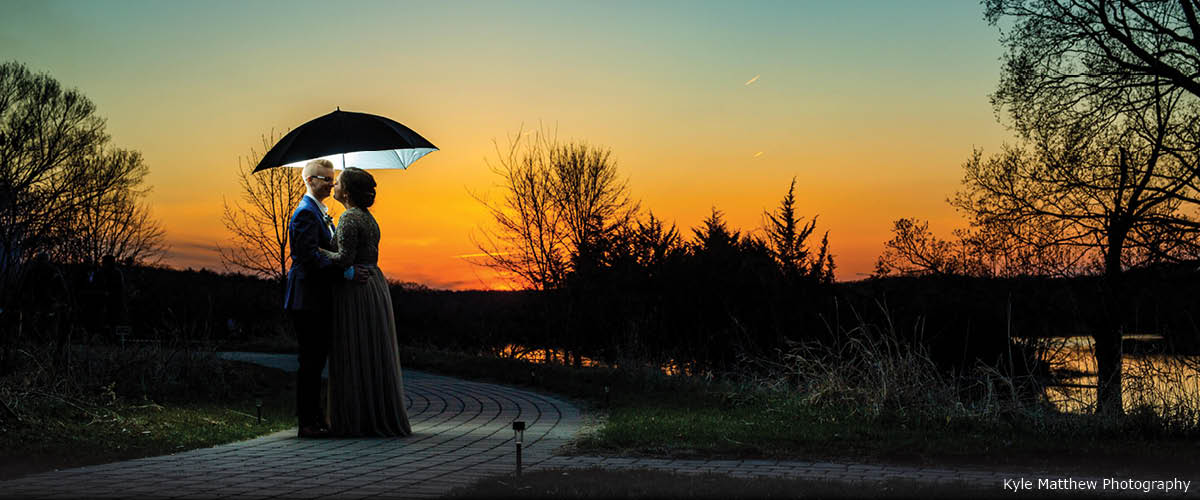A couple poses at sunset under an umbrella.