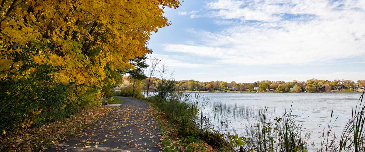 A paved trail winds past a lake in the fall.