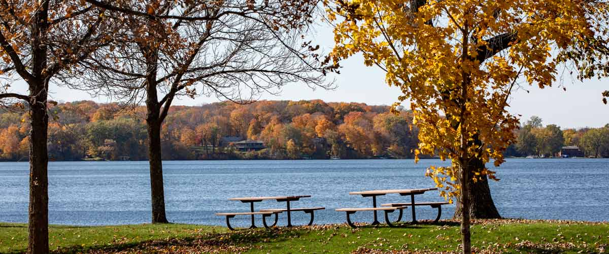 Two picnic tables overlook a lake in the fall/