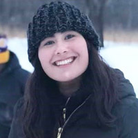A young woman with long black hair in a black winter hat and coat smiles.