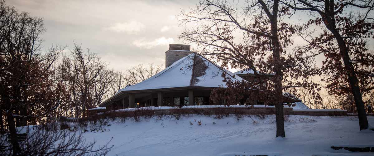 A circular visitor center is silhouetted by sunset on a snowy day.