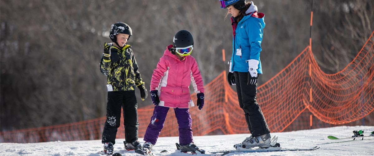 A ski instructor teaches two young kids how to downhill ski.