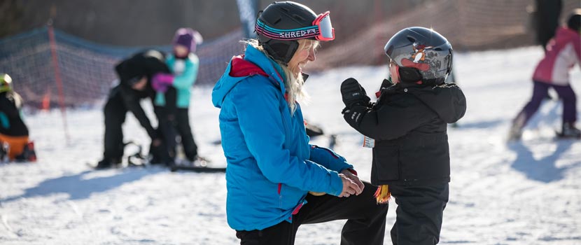 A woman ski instructor teaches a young boy how to downhill ski.