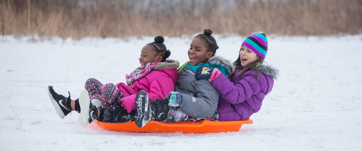 Three girls smile after sledding down a hill.