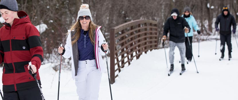 Several people cross-country ski over a bridge.