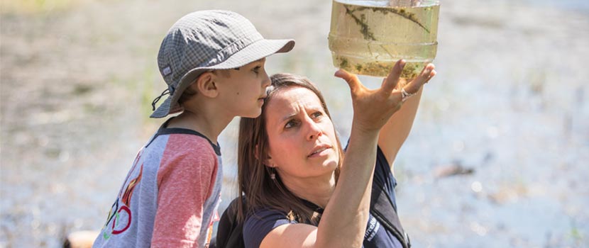 A naturalist shows a jar of pond water to a young boy.