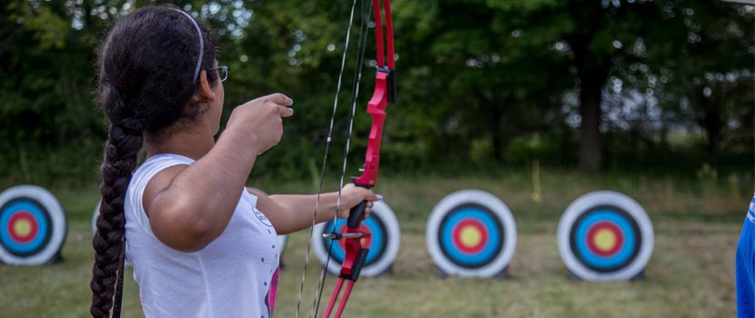 A woman aims a bow and arrow at a target.