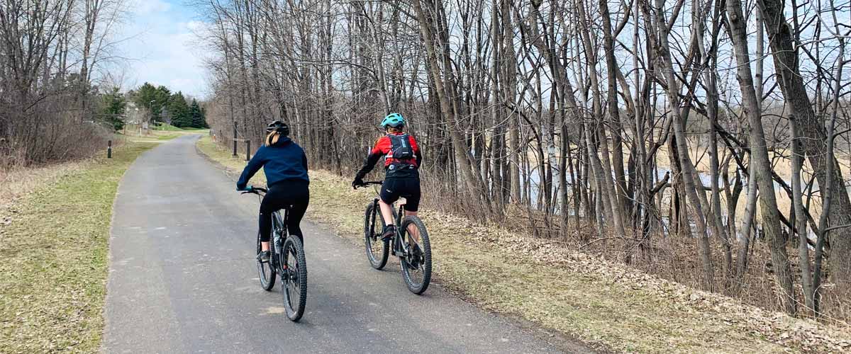 Two bikers ride down a paved trail along a river.