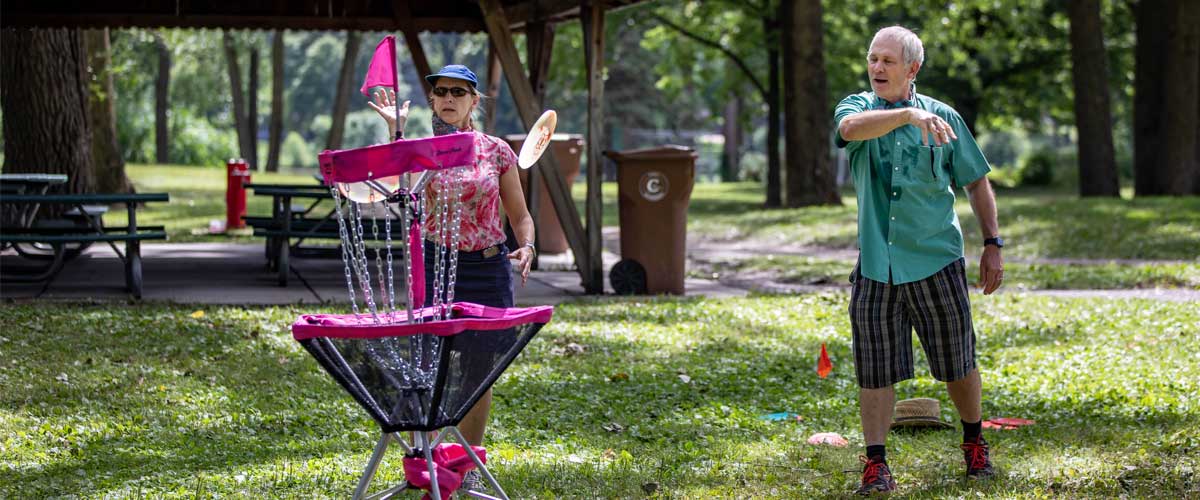 An older man and woman aim their discs at a basket.
