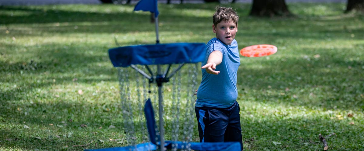 A young boy tosses a disc toward a basket.