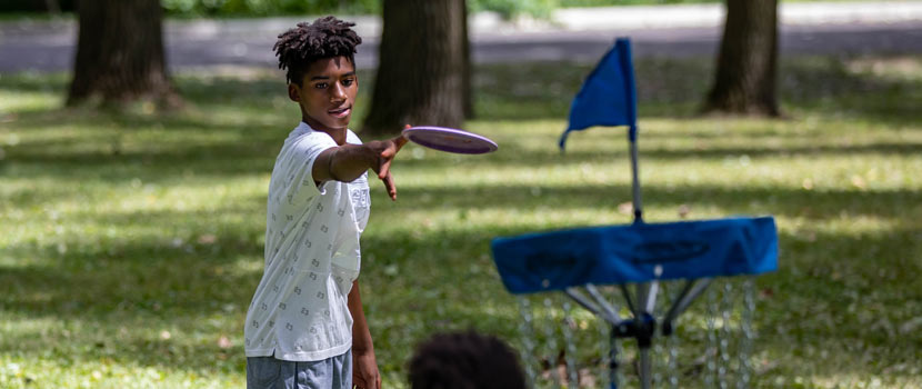 A boy aims a disc at a disc golf golf basket.